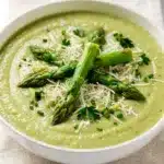 Creamy asparagus soup with Parmesan cheese in a white ceramic bowl.
