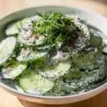 Creamy dill cucumber salad in a bowl with fresh herbs and red onion.