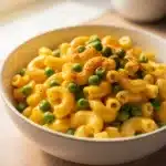 Creamy mac and cheese with peas in a bright home kitchen scene.