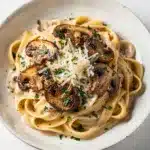 Creamy mushroom pasta with fettuccine, Parmesan, and herbs in overhead view.