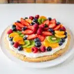 Colorful fresh fruit pizza with creamy frosting on golden sugar cookie crust