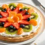Colorful fresh fruit pizza with cream cheese frosting on a rustic wooden board.