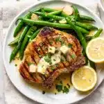 Golden garlic butter pork chops with green beans in a rustic skillet.