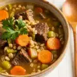 Hearty beef and barley soup with carrots and celery in a rustic bowl.