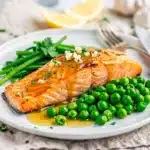 Honey mustard glazed salmon with bright green peas on a white plate.