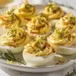 Lemon herb deviled eggs with creamy filling and fresh dill garnish on white platter.