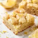 Golden lemon sugar cookie bars with crackly crust and bright glaze in ceramic dish.