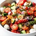 Cold rotini pasta salad with vegetables and cheese in a ceramic bowl.