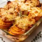 Golden brown scalloped sweet potatoes with creamy sauce and thyme garnish.