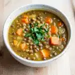 Simple lentil soup with carrots in a rustic ceramic bowl on wooden table