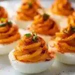 Smoky paprika deviled eggs with chives on a rustic slate board.