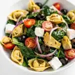 Colorful tortellini pasta salad with spinach and vegetables in a white bowl.