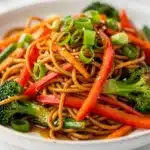 Colorful vegetable stir fry noodles in a glossy savory sauce with chopsticks