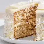 Close up slice of coconut cake with cream cheese frosting on plate.