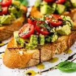 Creamy avocado bruschetta on toasted baguette with cherry tomatoes.