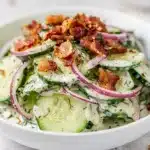 Creamy cucumber salad with bacon and fresh dill on a white plate.