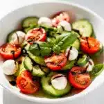 Fresh cucumber caprese salad with tomatoes, mozzarella, and basil in a bowl.