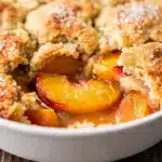Fresh peach cobbler with golden biscuit topping and cream.