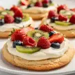 Colorful fruit pizza sugar cookies with creamy frosting on a bright plate.