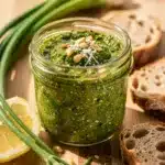 Vibrant garlic scape pesto in a rustic bowl with a wooden spoon.