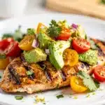 Grilled chicken topped with fresh avocado salsa on a white plate