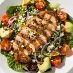 Grilled chicken salad with fresh vegetables and feta cheese in a rustic bowl.
