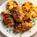 Glazed Huli Huli chicken thighs with pineapple on a white ceramic plate.