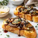 Close up of glossy mushroom bruschetta on rustic wooden board.