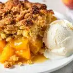 Golden brown peach cobbler dump cake with vanilla ice cream in ceramic bowl