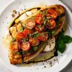 Pesto bruschetta chicken with melted mozzarella on a rustic wooden board.