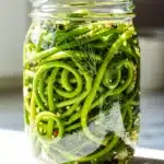 Crisp pickled garlic scapes in a jar on a rustic wooden table